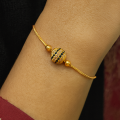 Gold bracelet with a decorative bead on a wrist, against a blurred background.