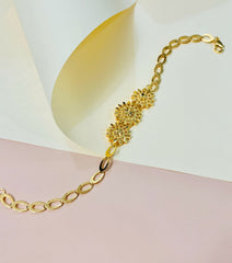 Gold bracelet with floral design on a soft pink and yellow background
