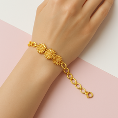 Gold bracelet with sunflower designs on a hand against a light pink background