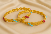 Pair of gold braided bracelets with colorful beads on a beige fabric background