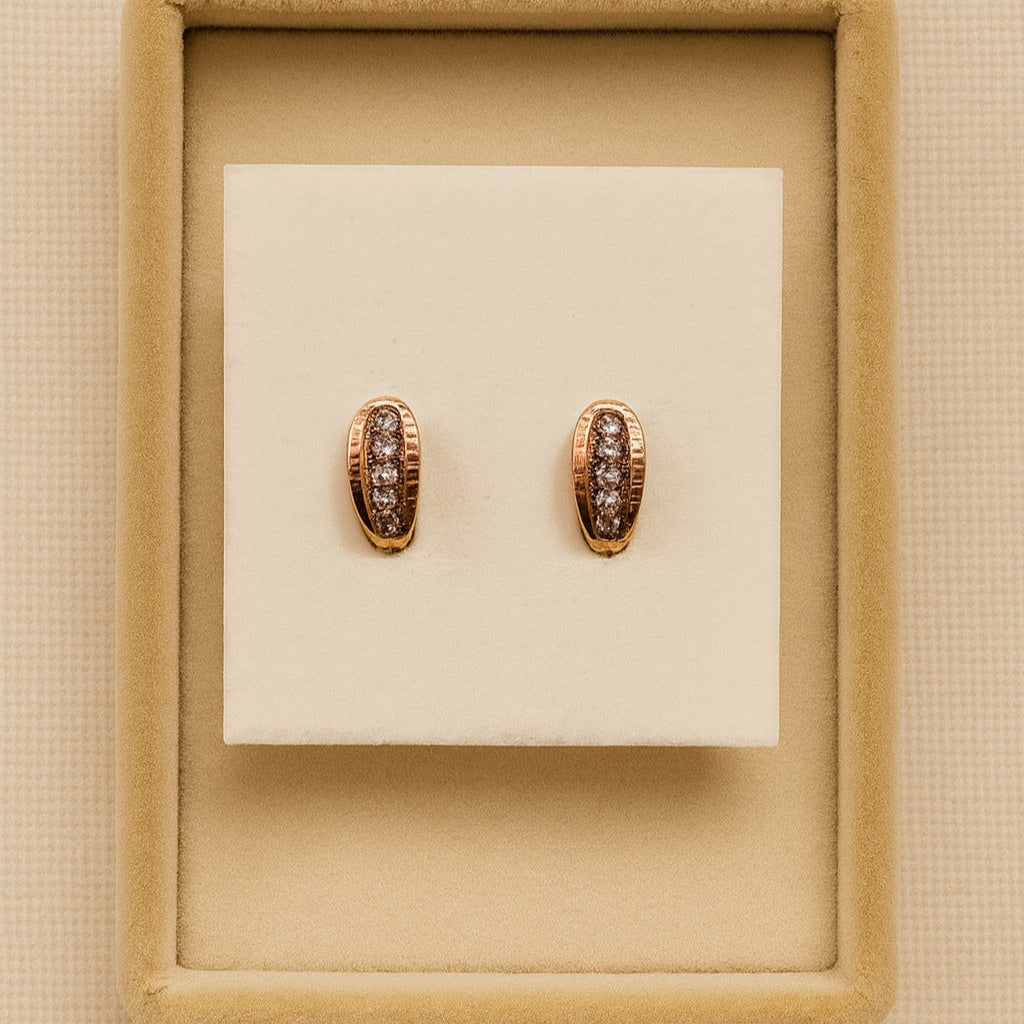 Pair of rose gold earrings with brown gemstones on a beige display box.