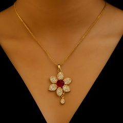 Gold necklace with a floral pendant featuring a red gemstone on a black background