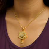 Gold necklace with a floral pendant on a person wearing a purple top.