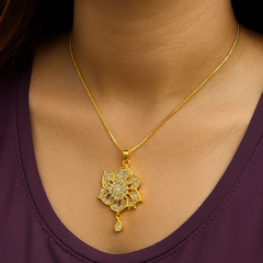 Gold necklace with a floral pendant on a person wearing a purple top.