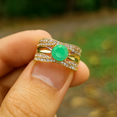 Gold ring with a green gemstone held by a hand against a blurred natural background