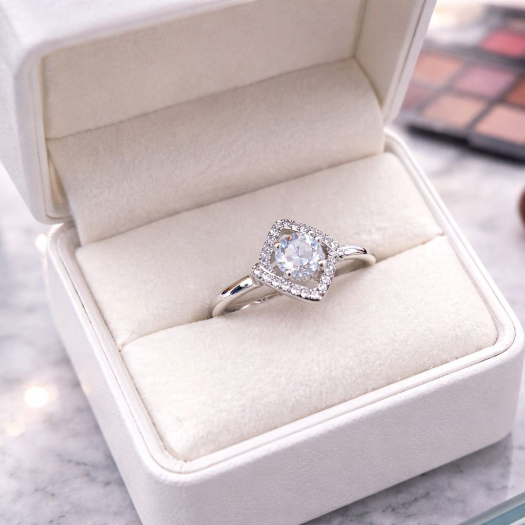 Silver ring with a diamond in an open jewelry box on a marble surface with makeup items.