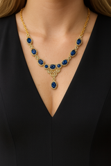 Gold necklace with blue gemstones worn by a person in a black outfit