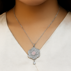 Silver necklace with a floral pendant on a person wearing a beige top.